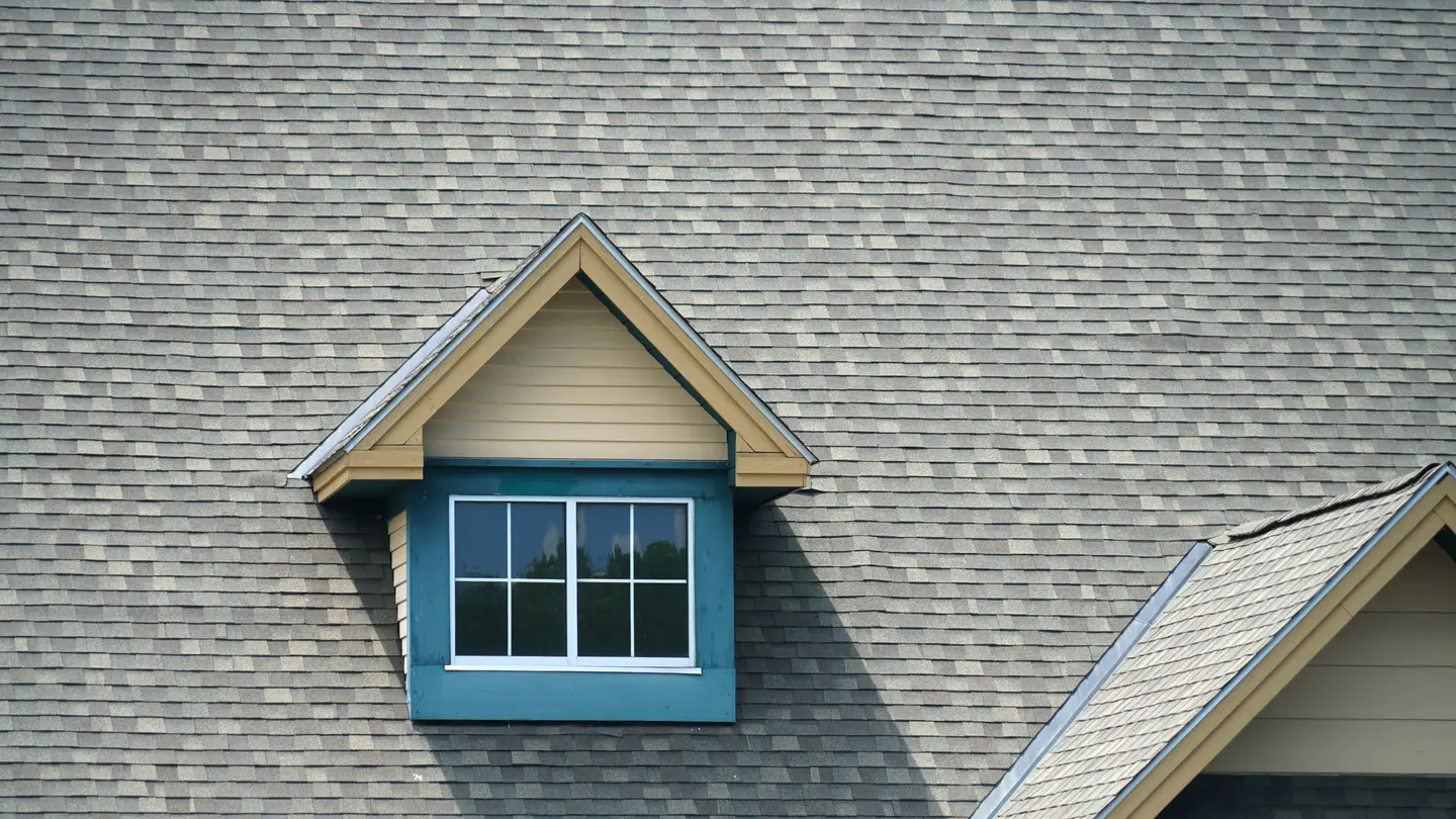 A closeup of a gray roof on a house with a window on the roof.