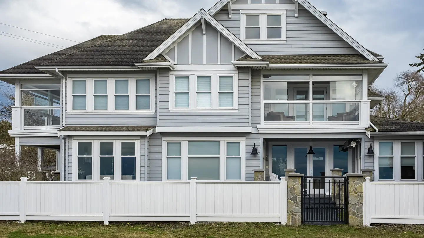 A two-story home with gray vinyl siding, white windows, and a white fence
