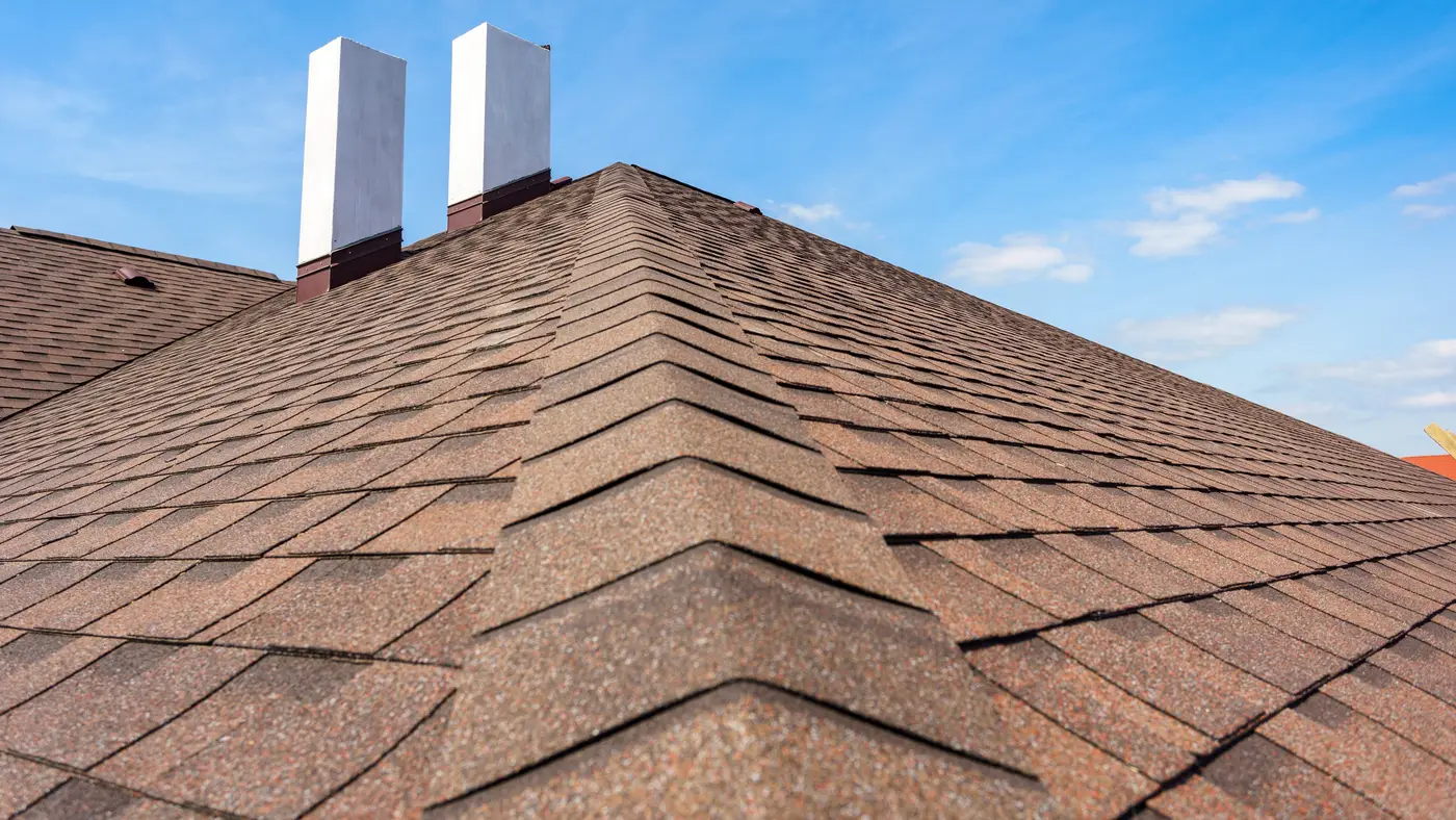 The roof of a multi-level house with a chimney and brown shingles in Marlton, NJ, by Ameritech Services.