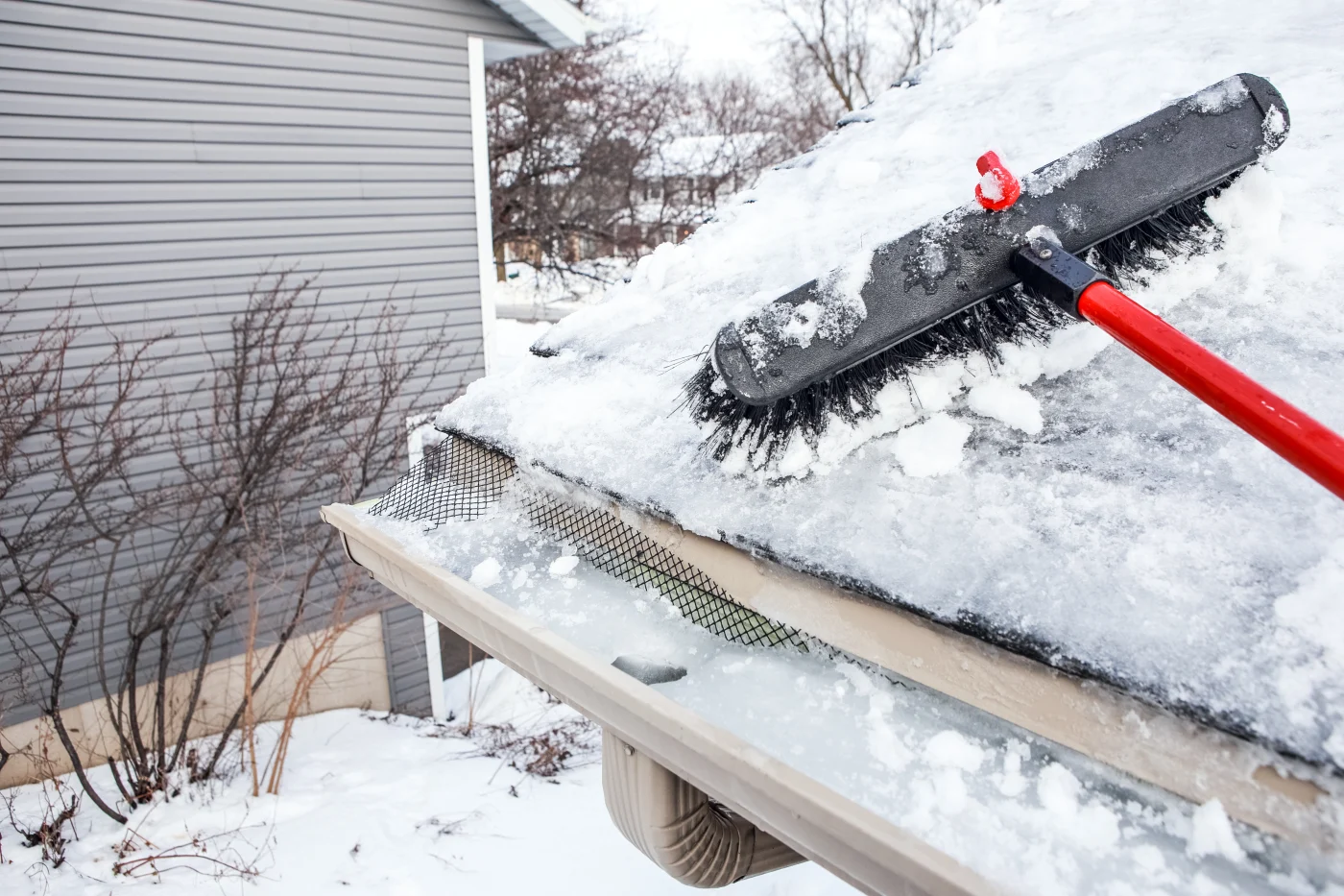 Adobestock 313533792 A brush removing snow off of a roof damaged by hail, snow, and ice in New Jersey.