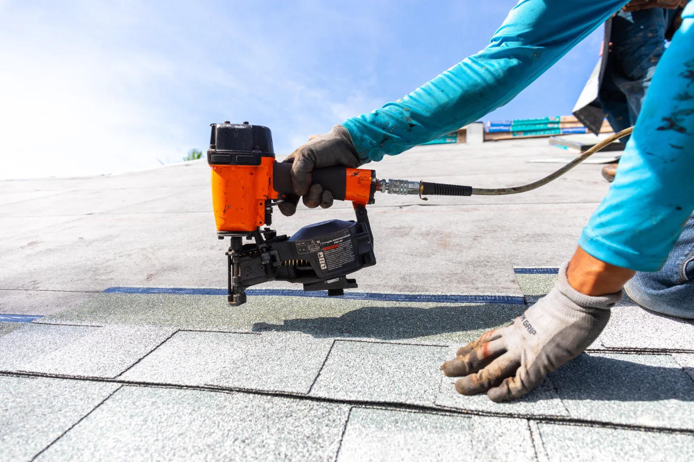 An Ameritech Services New Jersey roofer is installing roof shingles with nail gun.