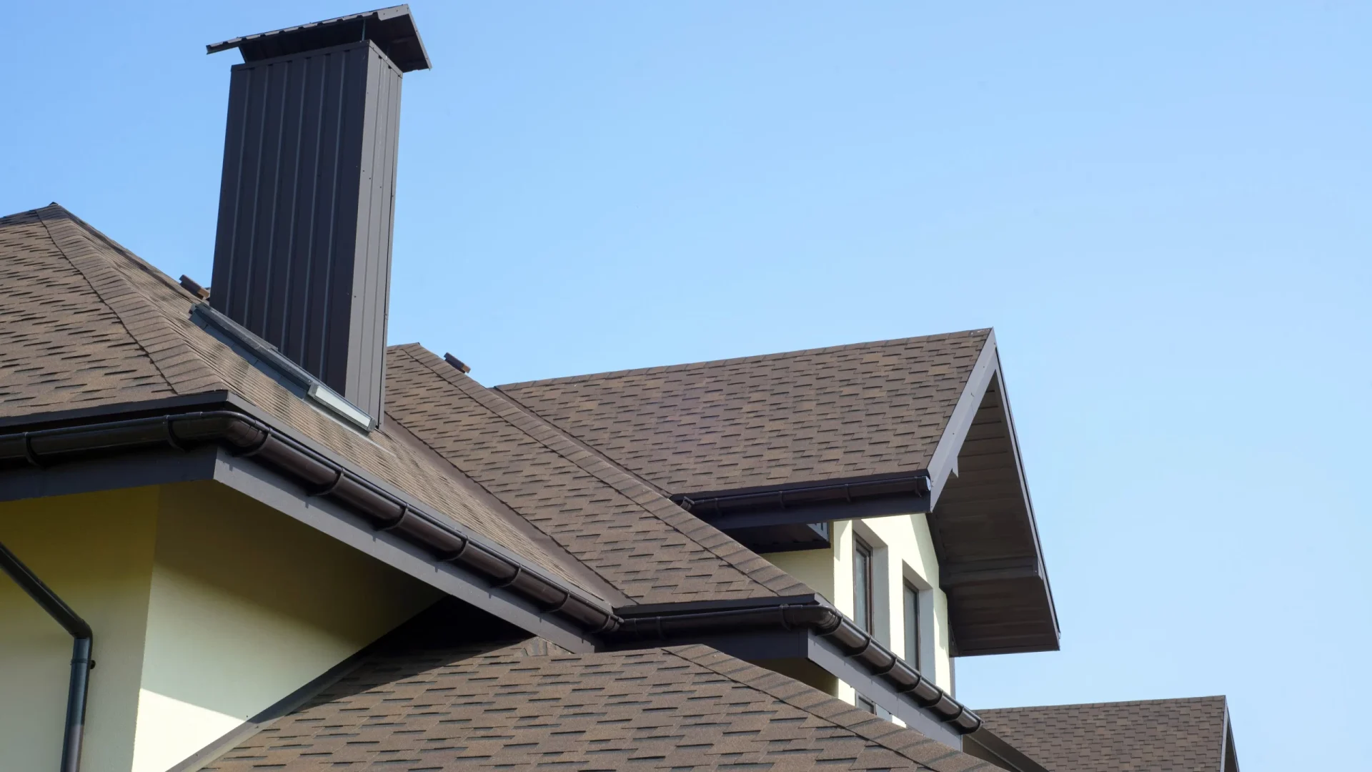 The roof of a multi-level house with a chimney and brown shingles in Marlton, NJ, by Ameritech Services.
