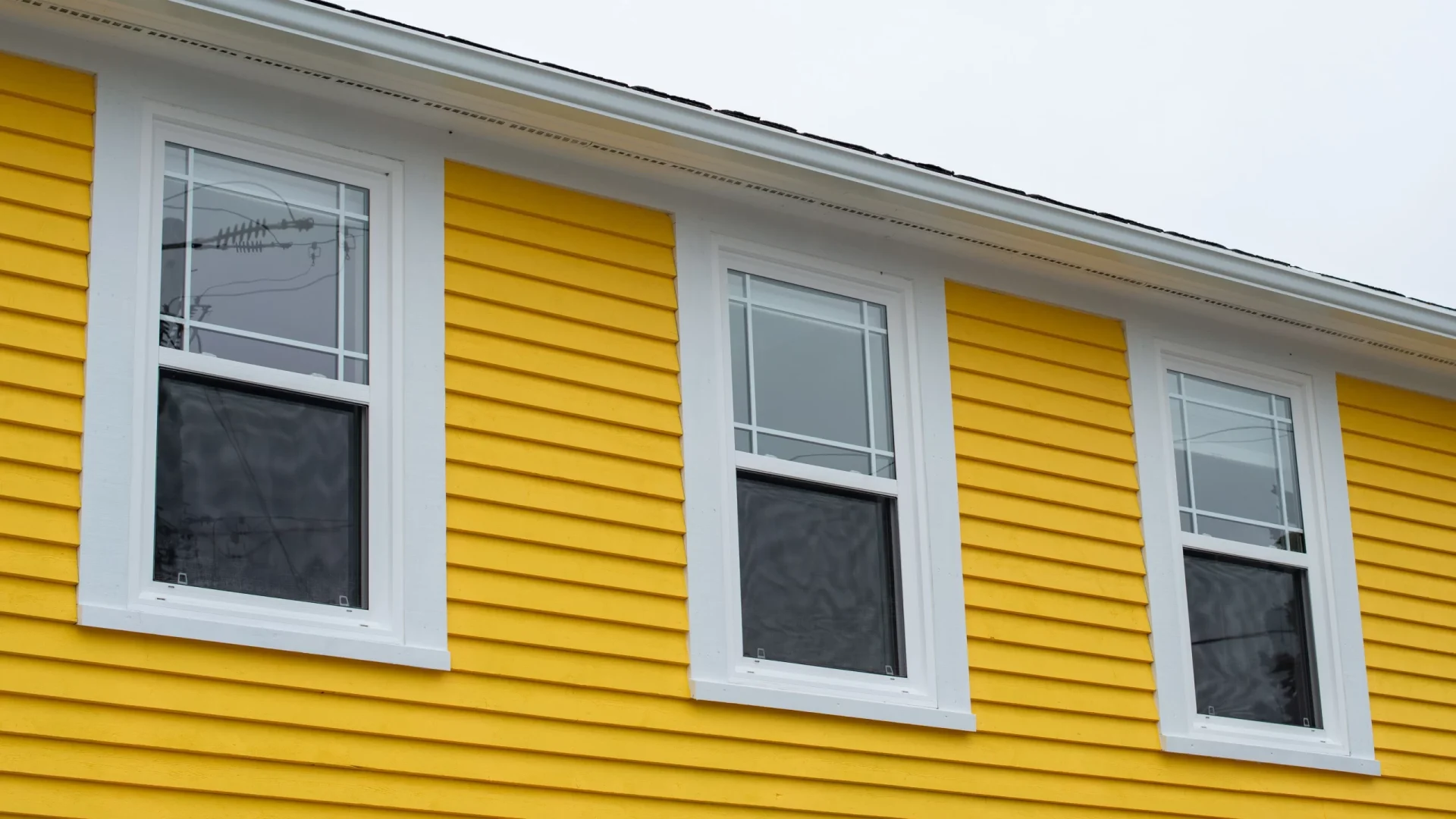 A closeup of a house with bright yellow siding with three windows with white trim in Sicklerville, NJ, by Ameritech Services