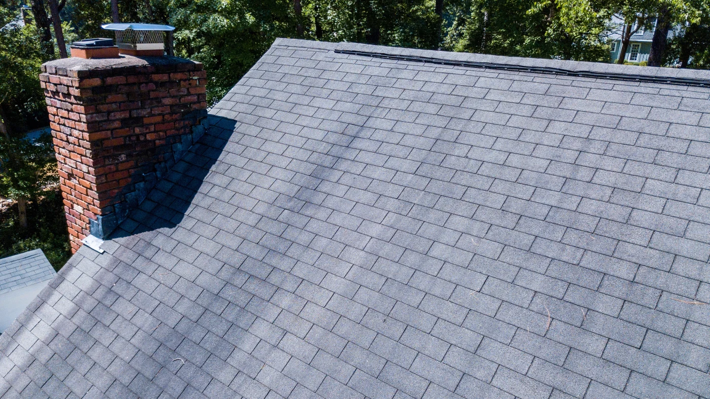 Closeup of a gray asphalt shingle roof with a red chimney