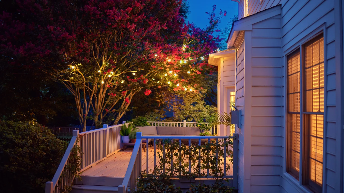 A home with light-colored siding and a small deck lit up with string lights