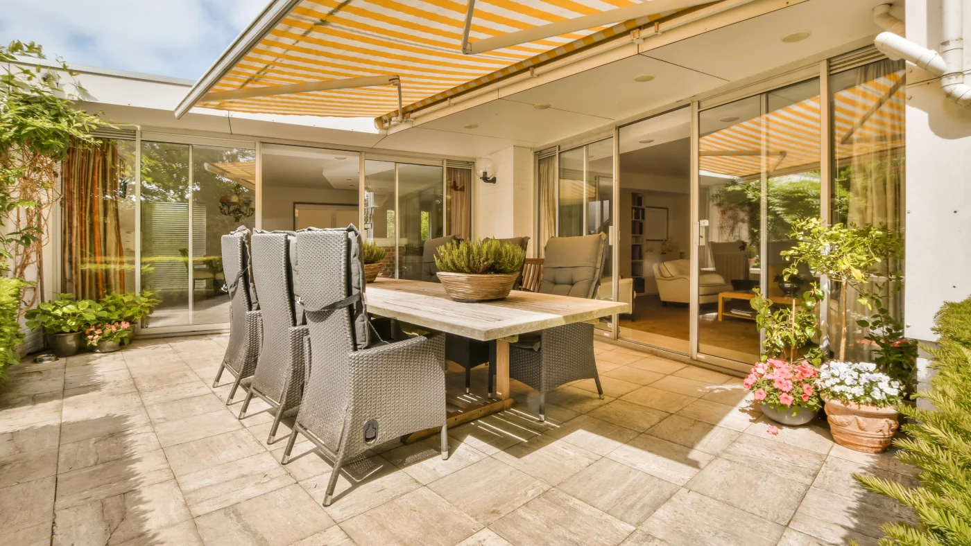 A patio with a full dining set and two patio doors leading into different rooms in the house
