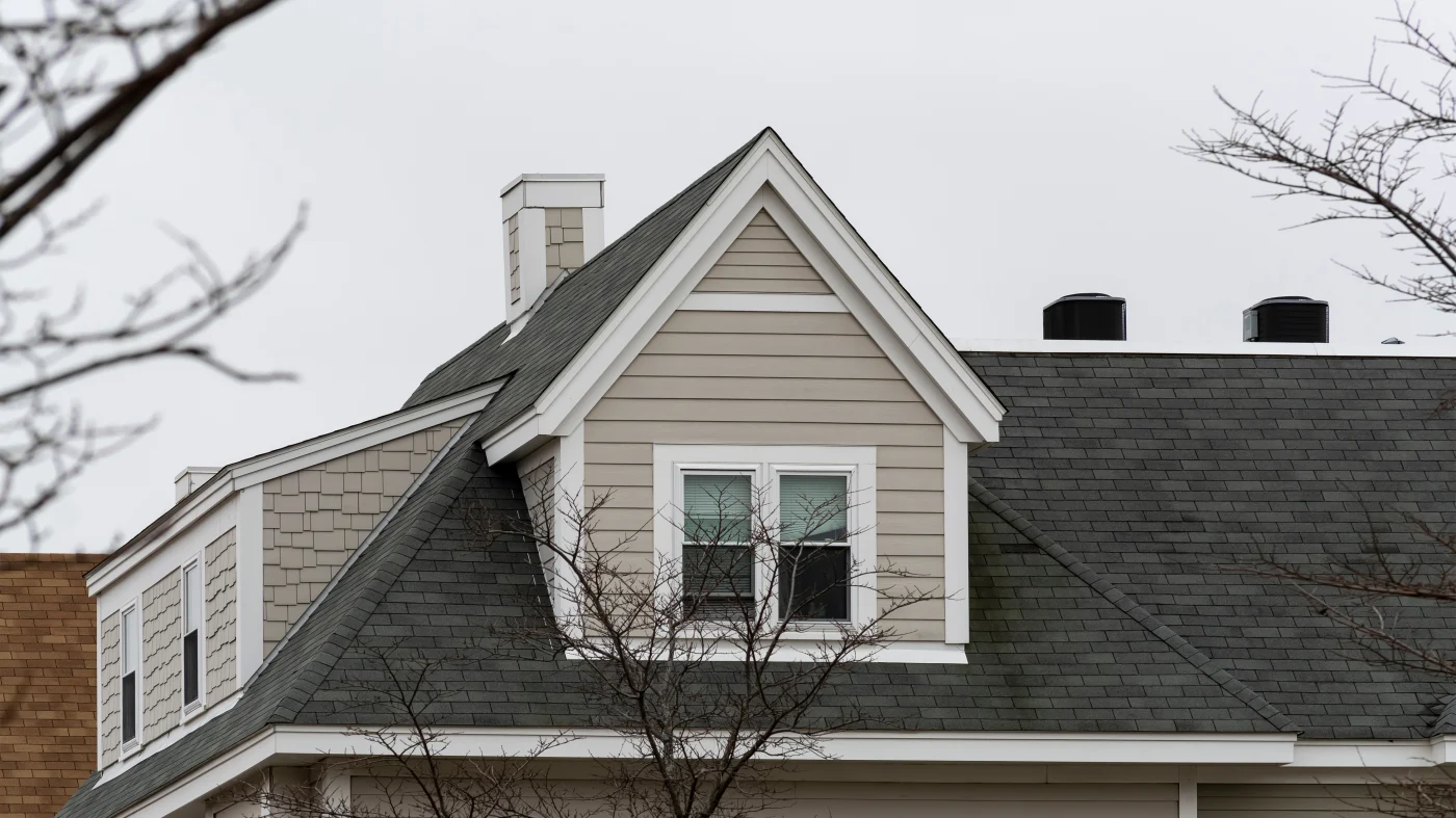 Closeup of a new gray asphalt roof on a tan-sided home