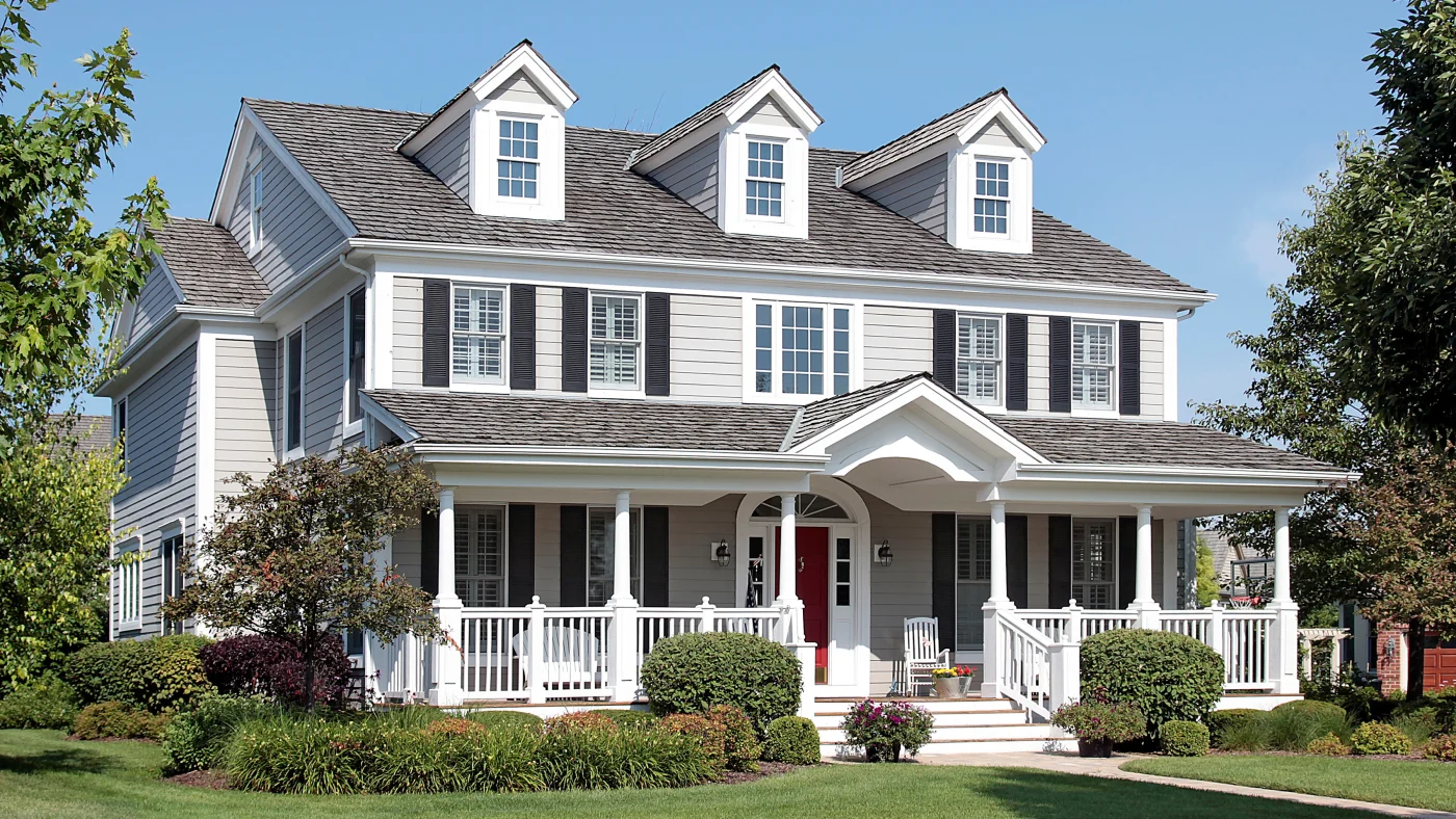 A two-story home with three attic dormers, white siding, and a cedar roof