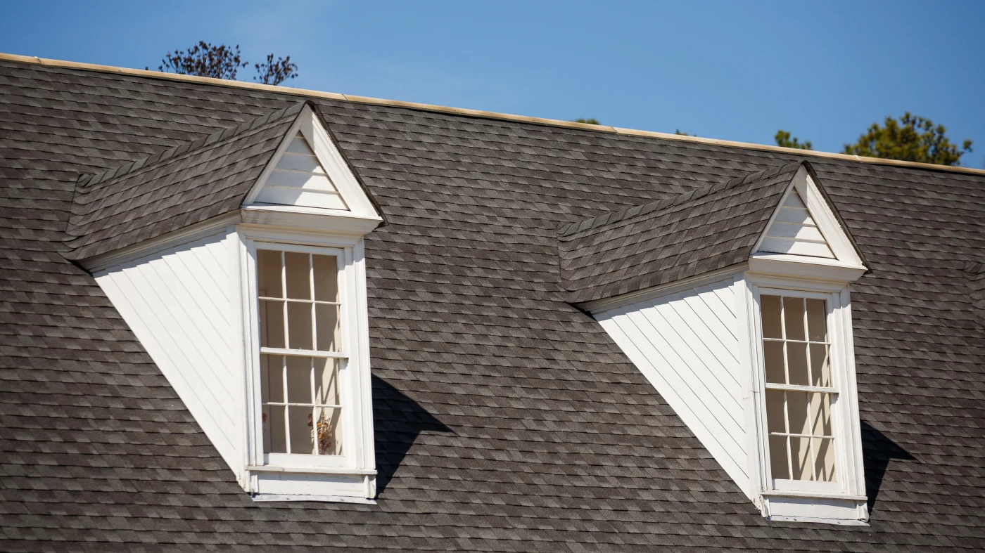 Closeup of a gray asphalt roof with two dormer windows