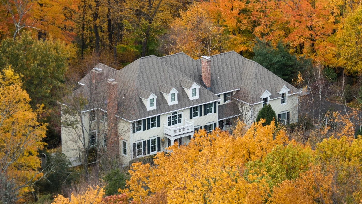 White single-family home with asphalt shingle roof among autumn trees