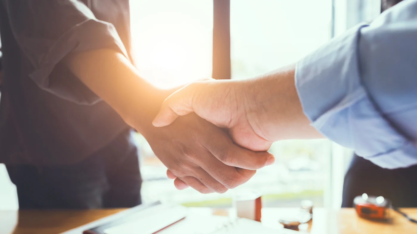 A homeowner and roofing contractor shake hands, agreeing to the contract