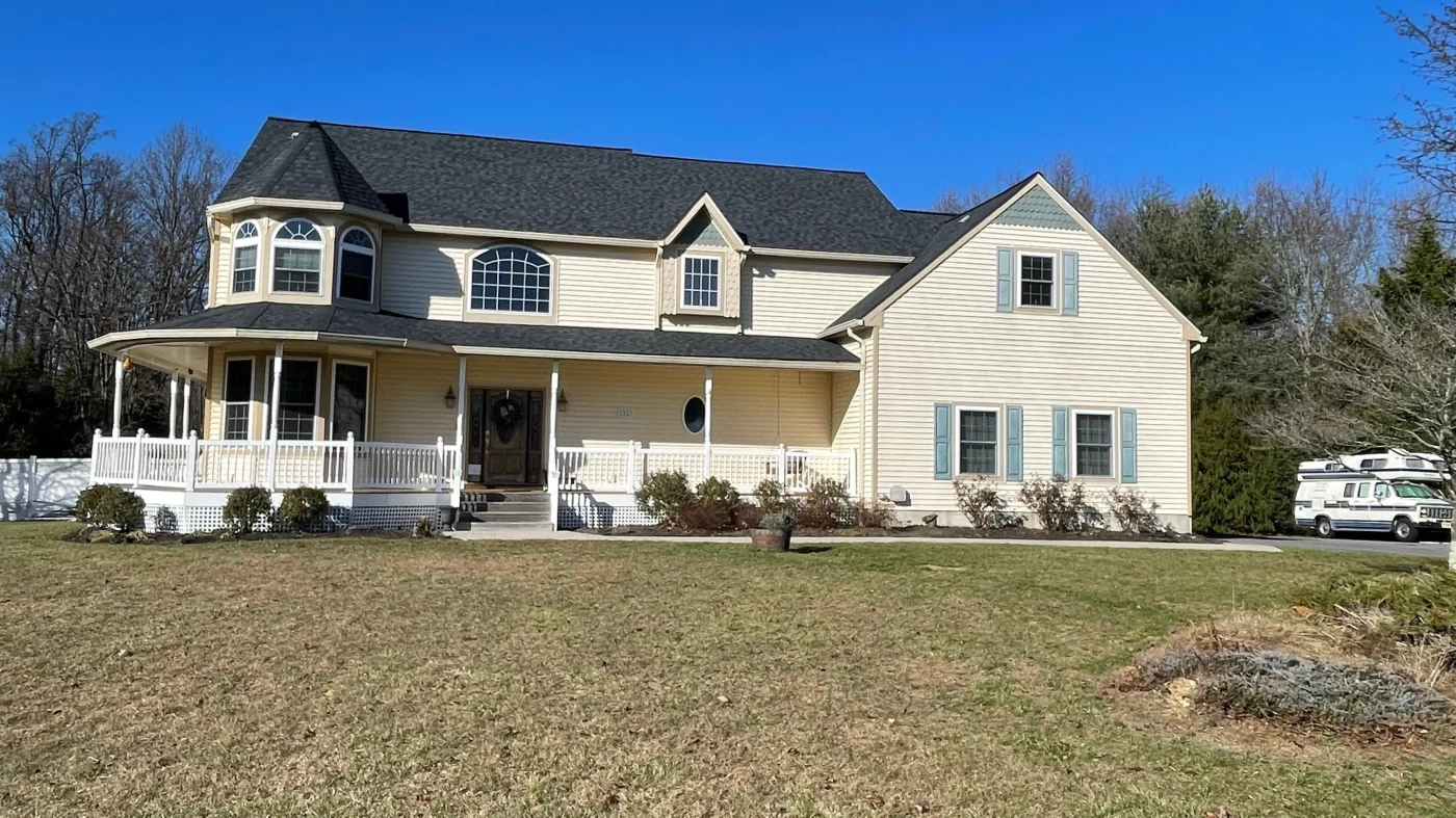 Large, two-story home with cream siding and black asphalt roofing