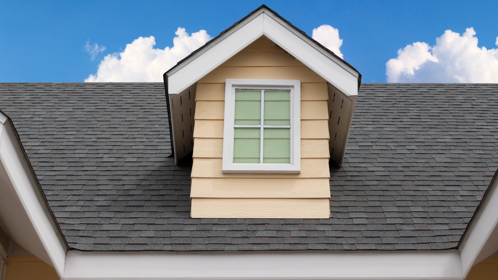 A closeup of a gray roof on a house with beige siding.