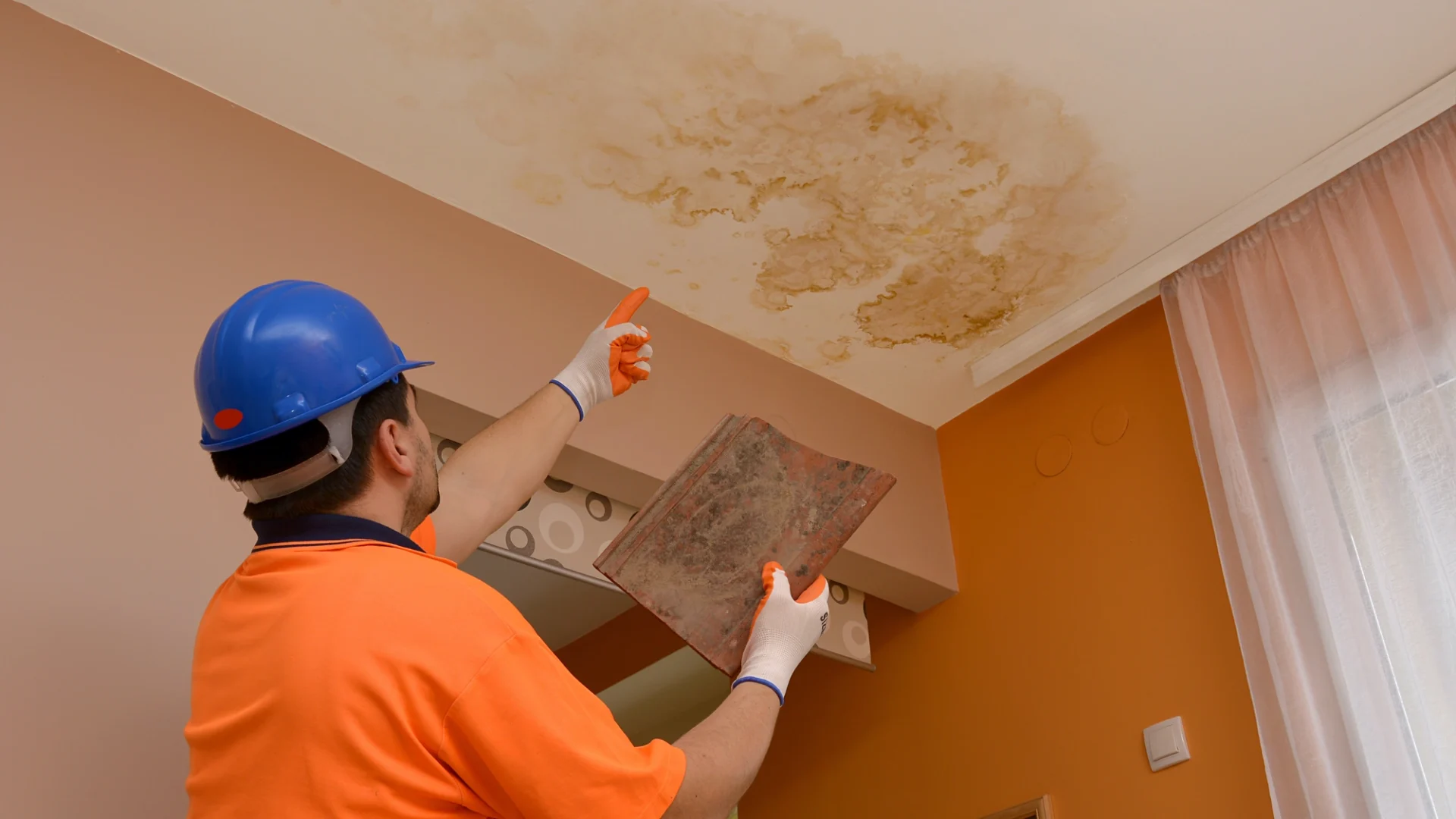 A contractor points at some water spotting on a ceiling as an indicator for roofing damage