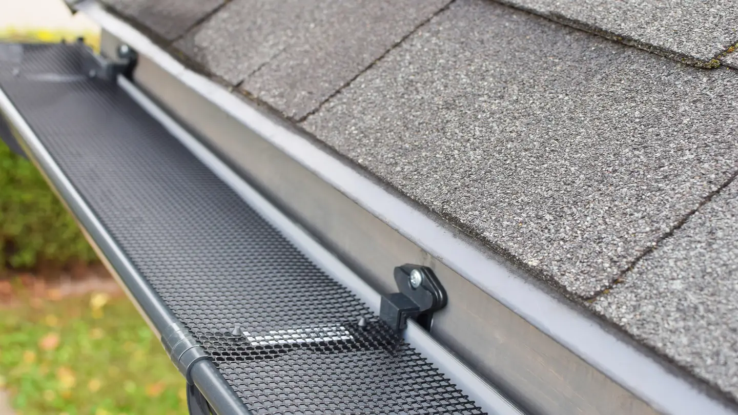 Closeup of the edge of an asphalt shingle roof with a gutter and mesh gutter guard system installed