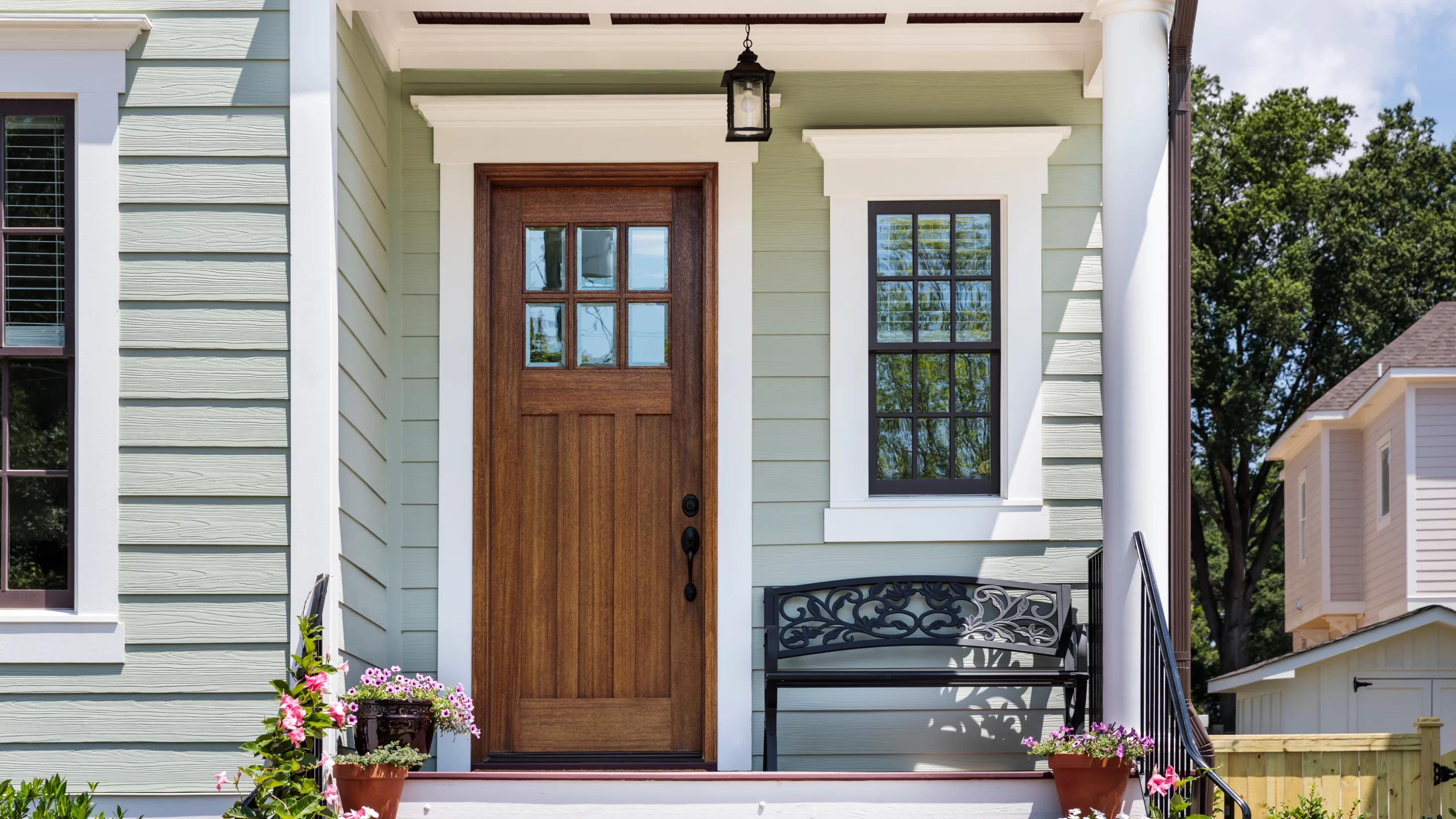 The front of a green-sided home with white trim and a brown wood entry door