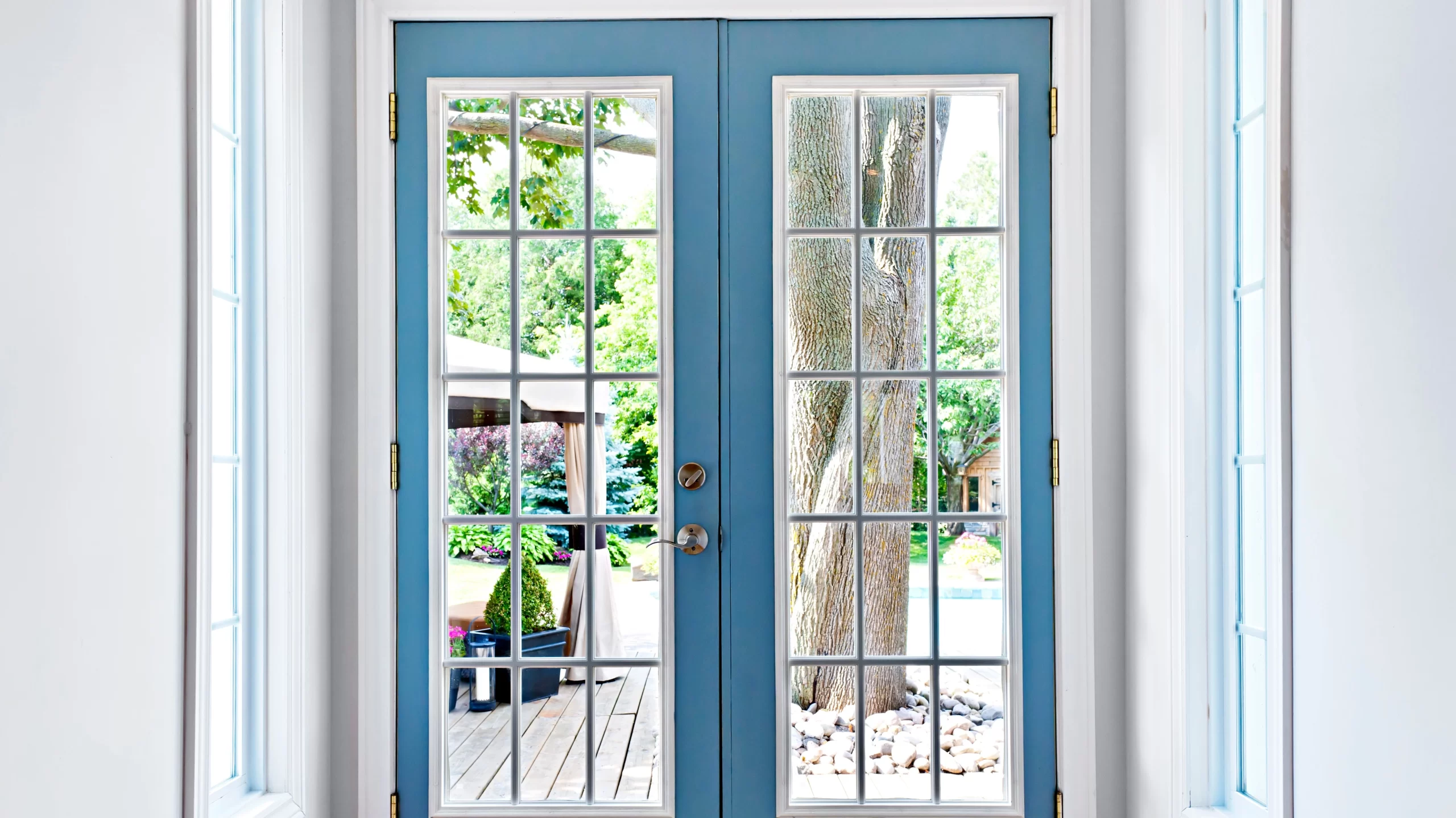 Closeup of blue French patio doors overlooking a deck and yard with a large tree and pergola