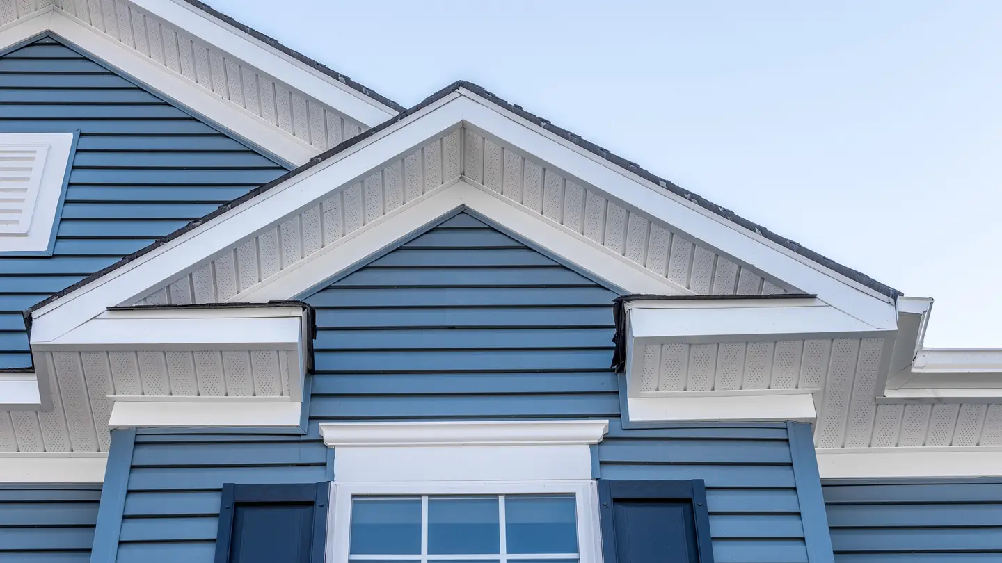 Closeup of a home with blue vinyl siding and white trim with blue sky in the background
