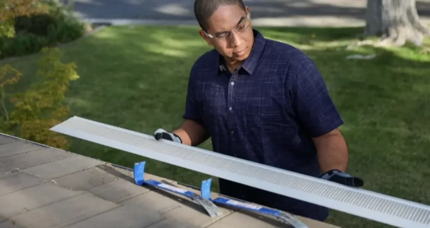 A man installing silver gutters and guards